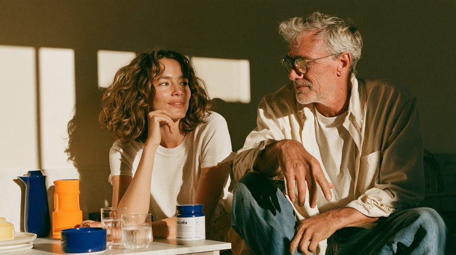 Two people talking together over drinks at a kitchen table.