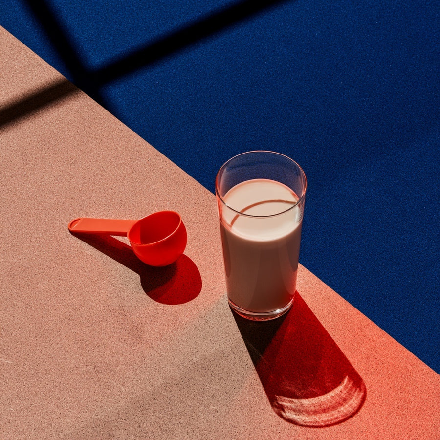 Glass of a creamy drink beside a red measuring scoop.