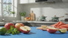 Apple, mint and lime being blended into a green smoothie and poured into a glass on a blue counter.